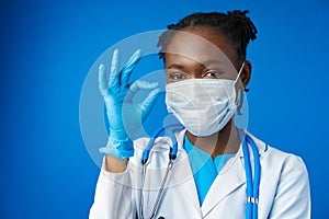 Portrait happy African American female doctor showing ok sign in blue studio