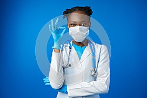 Portrait happy African American female doctor showing ok sign in blue studio