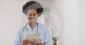 Portrait of happy african american female doctor using tablet, looking at camera and smiling
