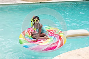 Portrait of happy african american girl with snorkel sitting on inflatable ring in swimming pool