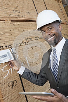 Portrait of happy African American male contractor using tablet PC while inspecting wooden planks