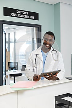 Portrait of happy african american male doctor wearing lab coat and stethoscope, holding laptop