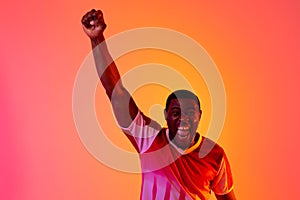 Portrait of happy african american male soccer player raising hand over neon pink lighting