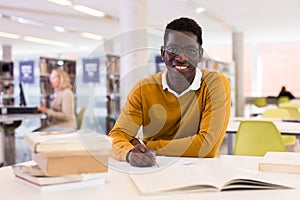 Portrait of happy african-american male student working with book in public library