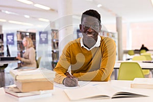 Portrait of happy african-american male student working with book in public library