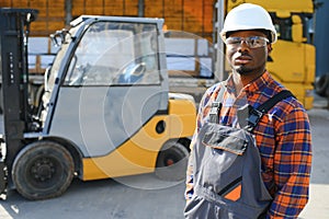 Portrait of a happy African American male worker driving forklift at workplace