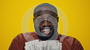 Portrait of happy African American man counting money on yellow background.