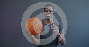 Portrait of happy African American man playing basketball enjoying sports game and looking at camera on gray background