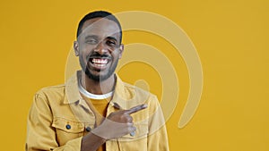 Portrait of happy African American man pointing sidewards and laughing on yellow background