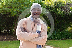 Portrait of happy african american man standing in garden wearing woolly hat and scarf