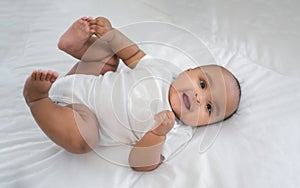 Portrait of happy African American mixed race cute girl baby lying down on white bed and look on camera in a bedroom at home