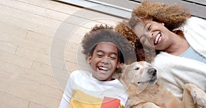 Portrait of happy african american mother and son lying on floor, with their pet dog, slow motion