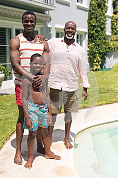 Portrait of happy african american multi-generational family standing at poolside on sunny day