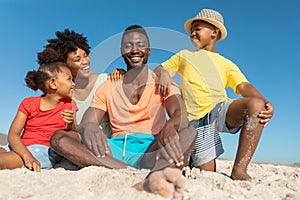 Portrait of happy african american parents and children on sand at beach against blue sky