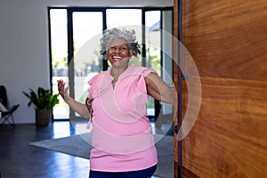 Portrait of happy african american senior woman welcoming while standing at doorway in nursing home