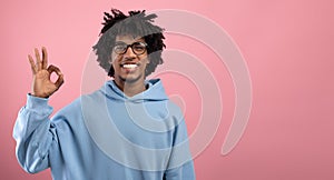 Portrait of happy African American teen guy showing OK gesture over pink studio background, panorama with blank space