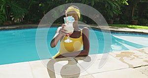 Portrait of happy african american woman standing in swimming pool making a toast with her drink