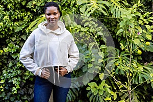 Portrait of happy african american woman in white hooded sweatshirt standing in garden, copy space