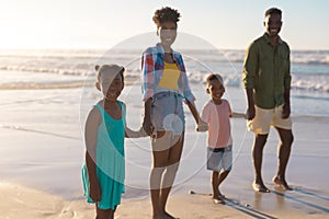 Portrait of happy african american young parents holding girl and boy\'s hands at beach against sky