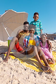 Portrait of happy african american young parents relaxing with son and daughter at beach against sky