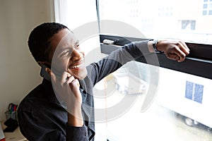 Happy african man looking out of window and talking on mobile phone