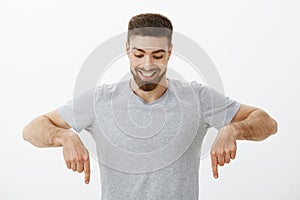 Portrait of happy and amazed good-looking masculine male with perfect hairstyle and beard looking and pointing down with