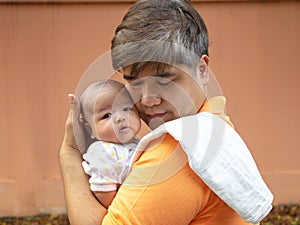 Portrait of happy Asia father holding his newborn sweet baby dressed in white clothes. The father embracing his baby with love and