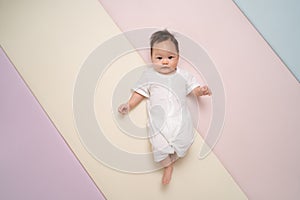 Portrait of happy asian baby infant in white laying down on pastel background with copy space