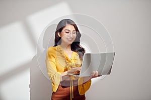 Portrait of a happy asian businesswoman holding laptop computer and looking away solated over white background
