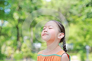 Portrait of happy Asian child close their eyes in garden with Breathe fresh air from nature. Close up kid girl relax in green park
