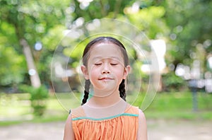 Portrait of happy Asian child close their eyes in garden with Breathe fresh air from nature. Close up kid girl relax in green park