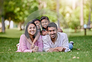 Portrait of happy asian family lying on grass in a park. Adorable little girls spending time with mom and dad on a