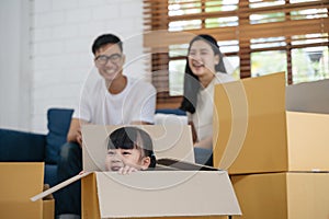 Portrait of happy Asian family moving to new house with cardboard boxes and playing cardboard box.