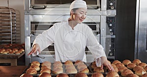 Portrait of happy asian female baker working in bakery kitchen, placing rolls on trays, slow motion