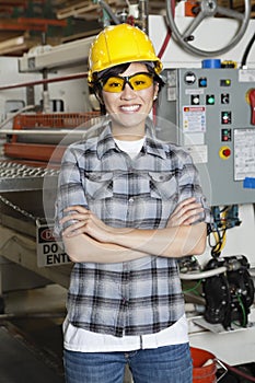 Portrait of happy Asian female industrial worker with machinery in background