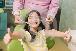 Portrait of happy asian girl shows thumb up gesture at dental clinic
