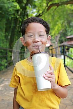 Portrait of happy Asian little boy child looking camera with sweating shirt holding paper cup and drinking cold water by straw