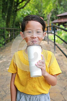 Portrait of happy Asian little boy child looking camera with sweating shirt holding paper cup and drinking cold water by straw