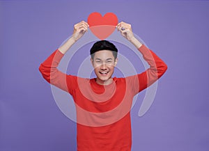 portrait Happy asian man holding red paper heart postcard dressed red clothes isolated on purple background. valentines day
