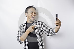 A portrait of a happy Asian man is smiling while holding on his phone, isolated by white background