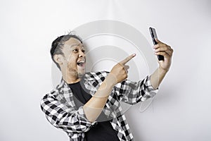 A portrait of a happy Asian man is smiling while holding on his phone, isolated by white background