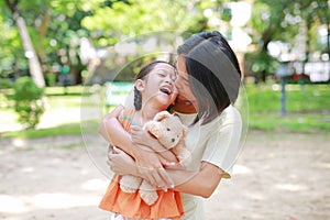 Portrait of happy Asian mother cuddle daughter and hugging teddy bear doll in the garden. Mom and child girl with love and