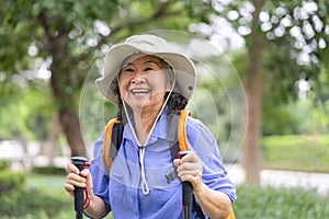 portrait happy asian senior woman with trekking poles and backpack wears hat in the national park for hiking
