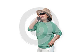 Portrait of happy asian senior woman wearing sunglasses, a hat, and holding smartphone standing isolated on white background.