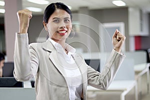 Portrait of happy Asian woman officer raising hands up to celebrate success, saying yes, extremely exciting feeling during