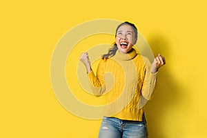 Portrait of a happy Asian woman screaming an excited and celebrating success isolated over yellow background. Succeed