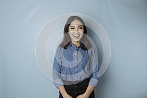 A portrait of a happy Asian woman is smiling and wearing a blue shirt isolated by a blue background