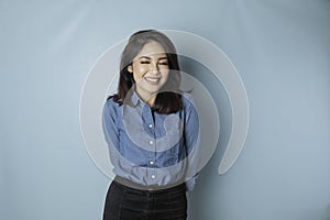 A portrait of a happy Asian woman is smiling and wearing a blue shirt isolated by a blue background