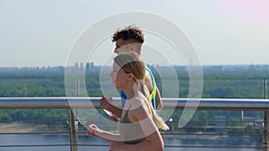 Portrait of happy athletic couple man and woman running on bridge with beautiful city landscape. Caucasian young