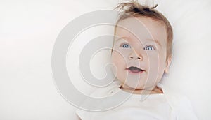 Portrait of happy baby boy lying on soft white pillow